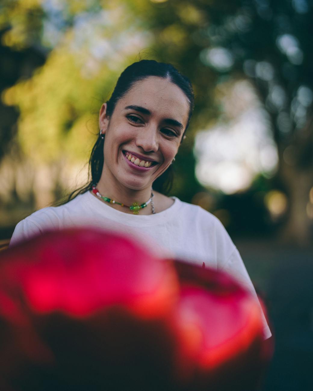 Smiling person holding a bouquet of red flowers outdoors.