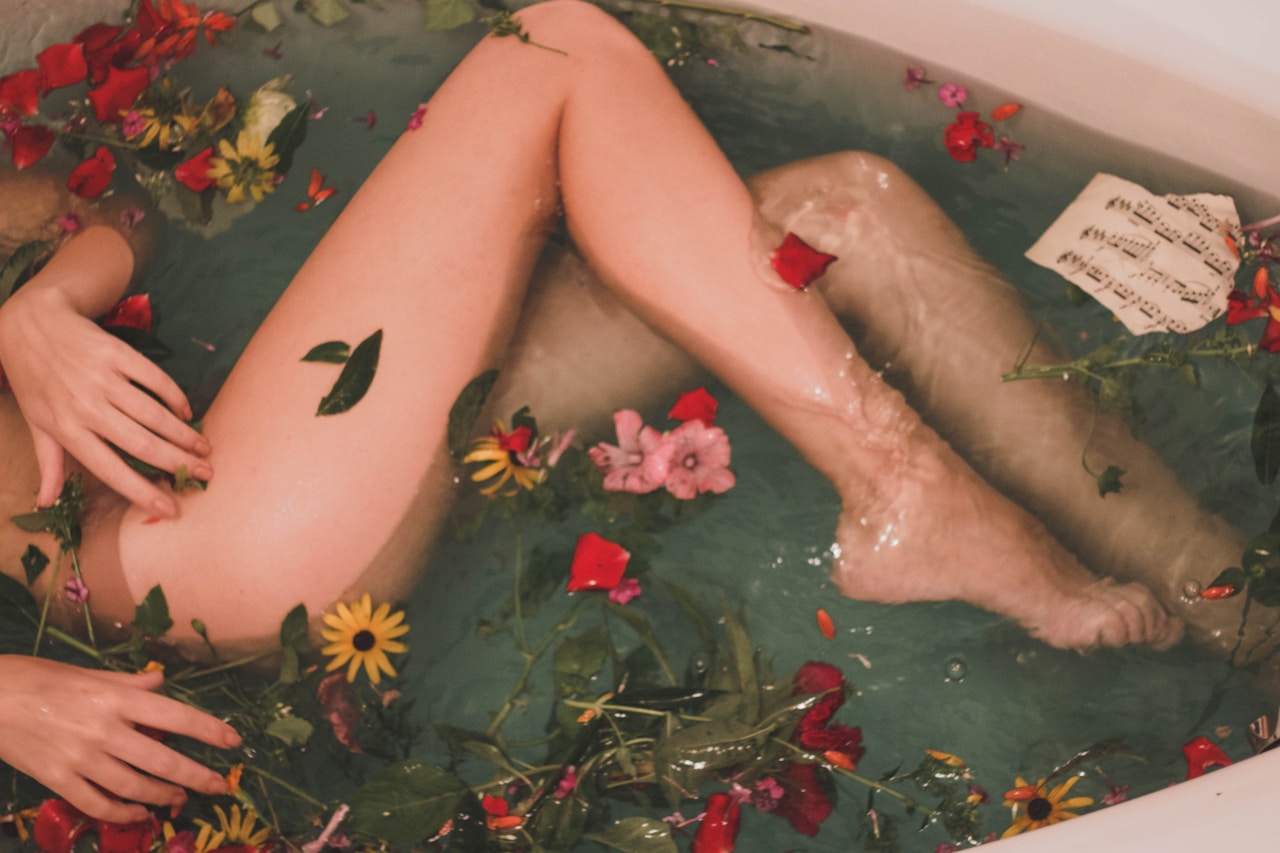 Person in bathtub with flowers and sheet music floating in water.