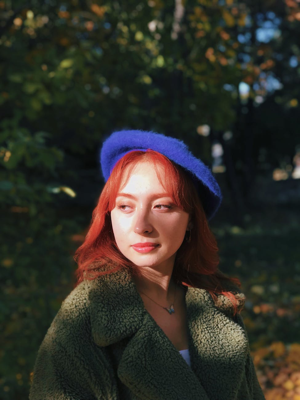 Woman with red hair and blue beret in a sunlit forest.
