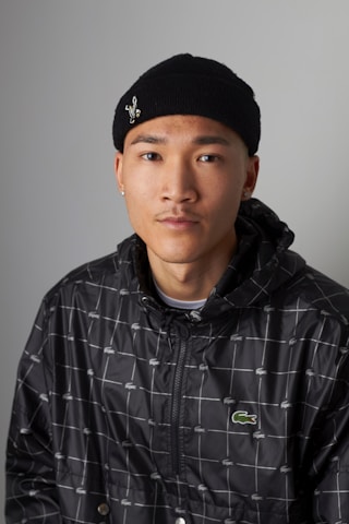 Person wearing a black beanie and patterned jacket against a gray background.