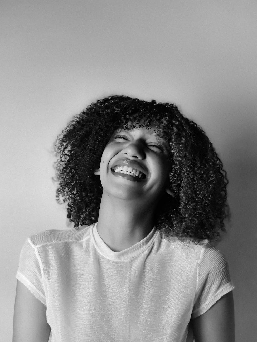 Black and white photo of a person laughing with curly hair.