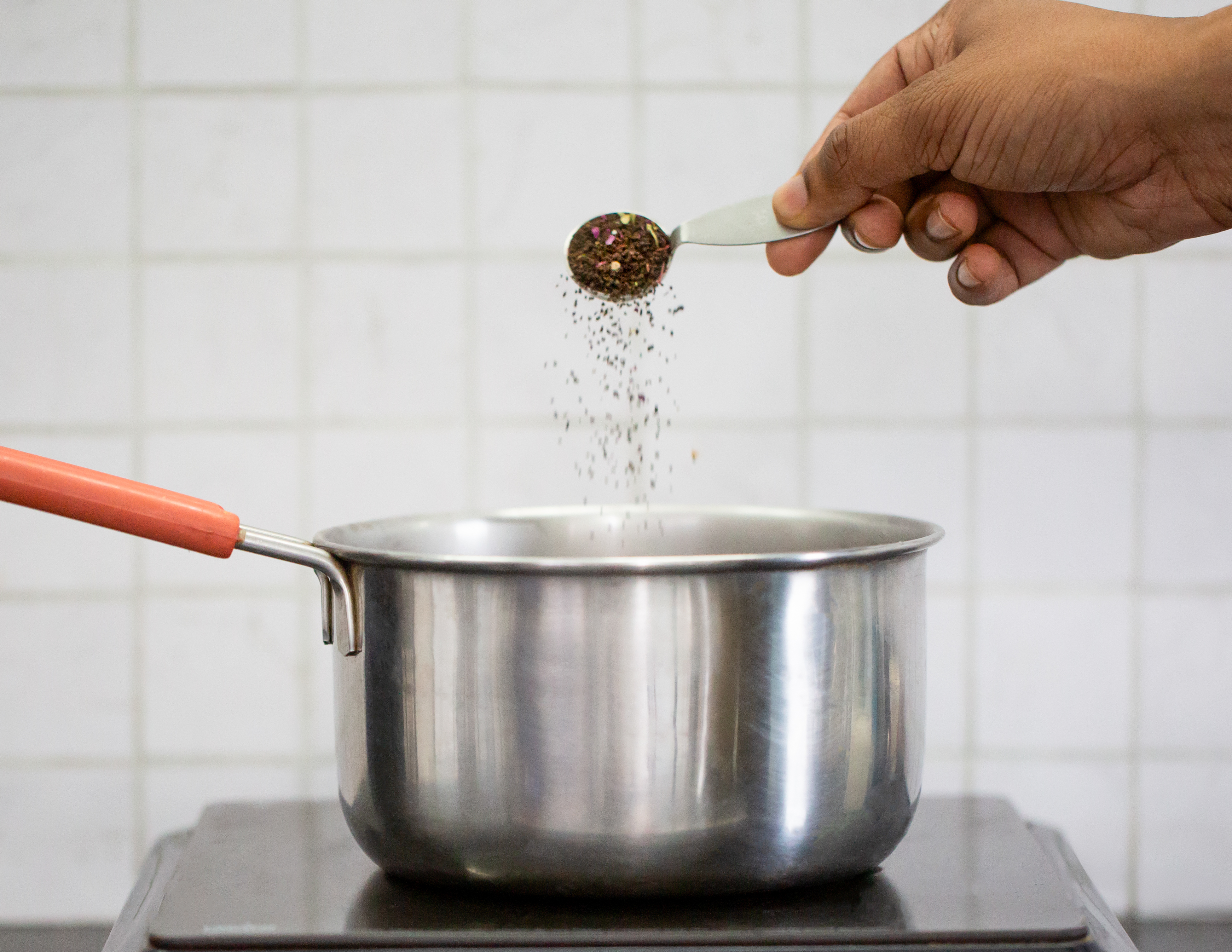 Hand adding spices into a stainless steel pot on the stove.