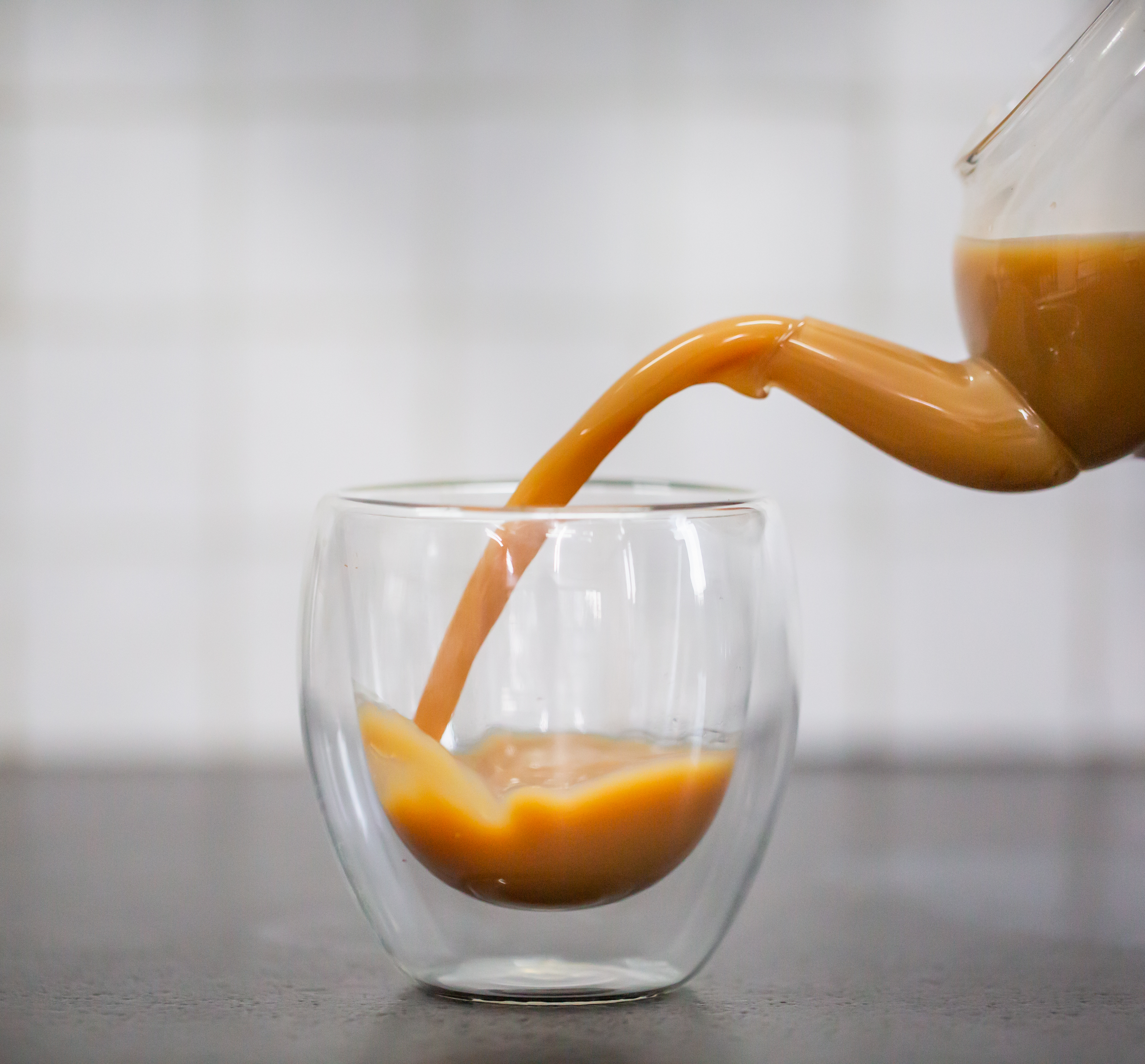 Pouring tea into a double-walled glass cup.