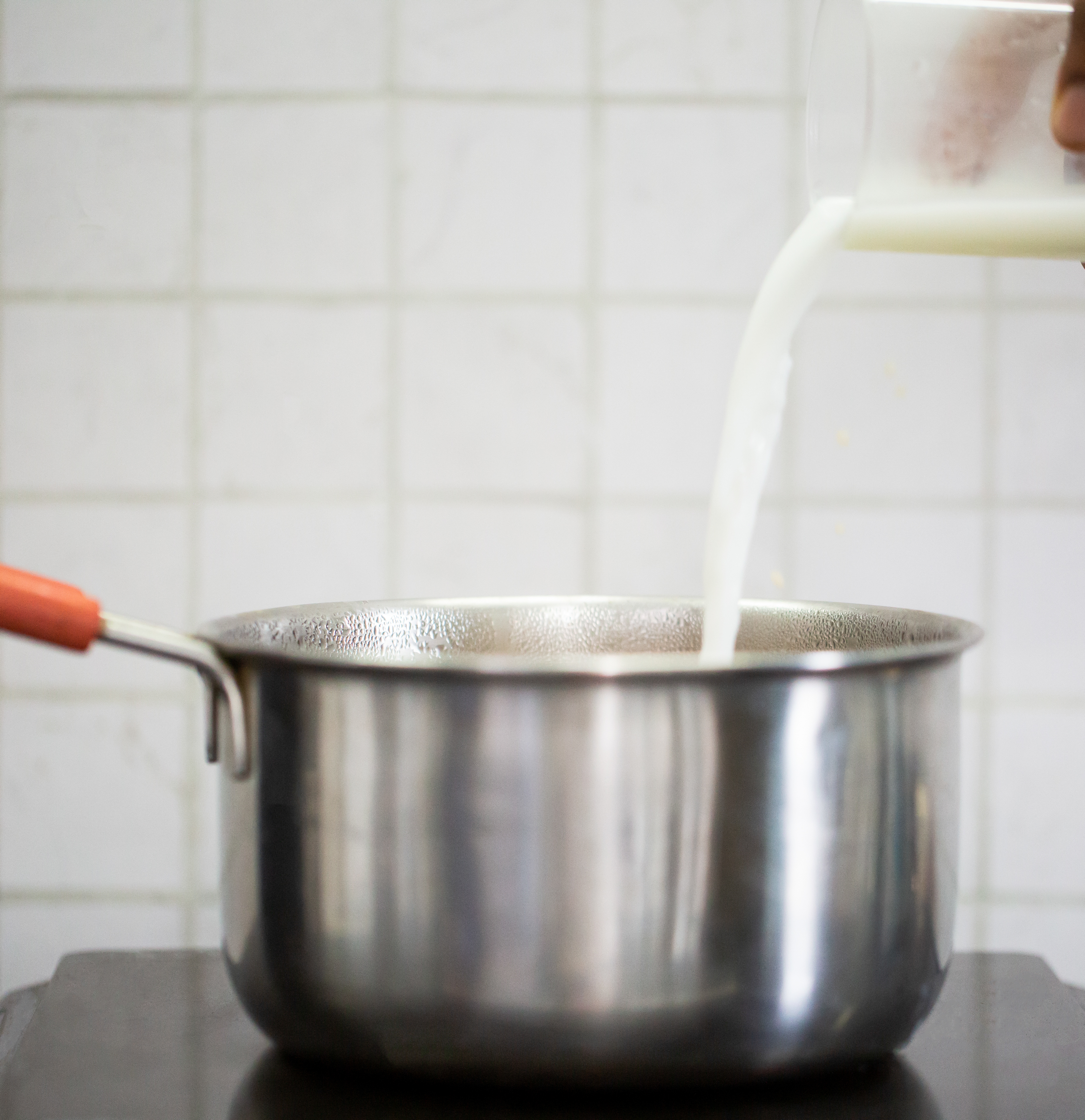 Pouring milk into a stainless steel pot on a stovetop.