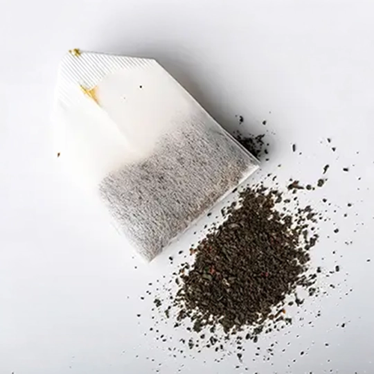 A single teabag on a white background with loose tea leaves spilled beside it.