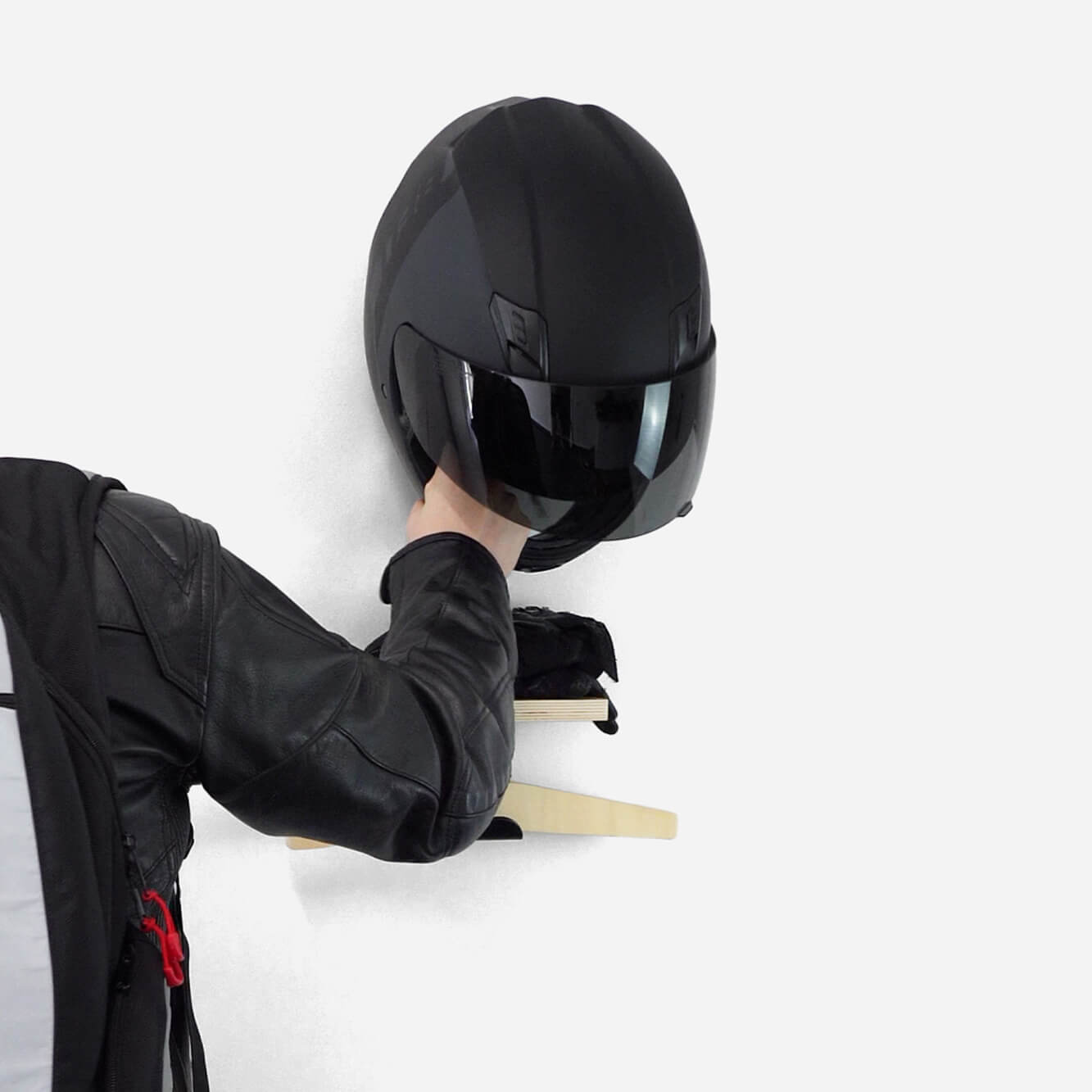 Person placing a black motorcycle helmet on a wall-mounted shelf.