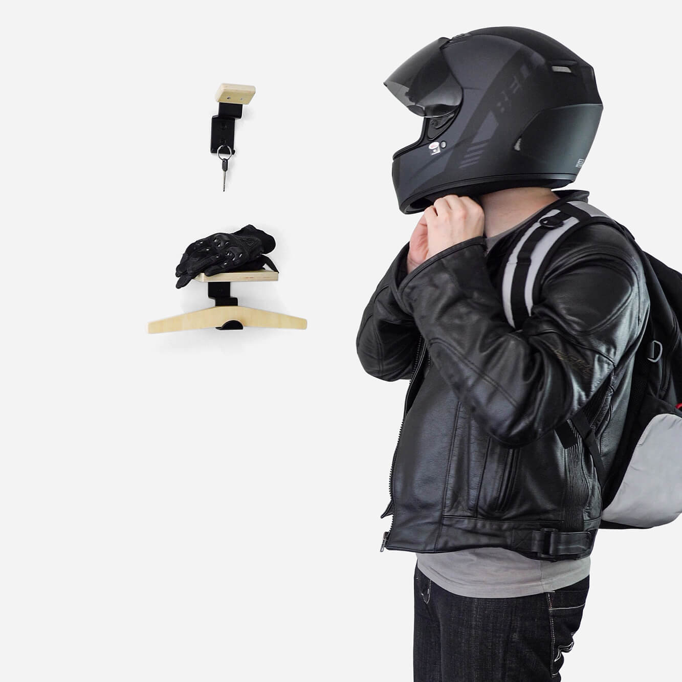 Person in motorcycle gear with helmet, standing by wall-mounted storage.