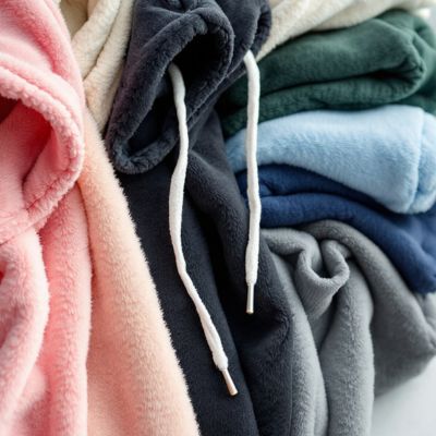 Pile of various colored fleece hoodies with drawstrings.