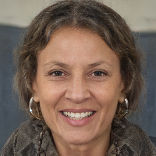 Smiling person with curly hair and hoop earrings, wearing a patterned scarf.
