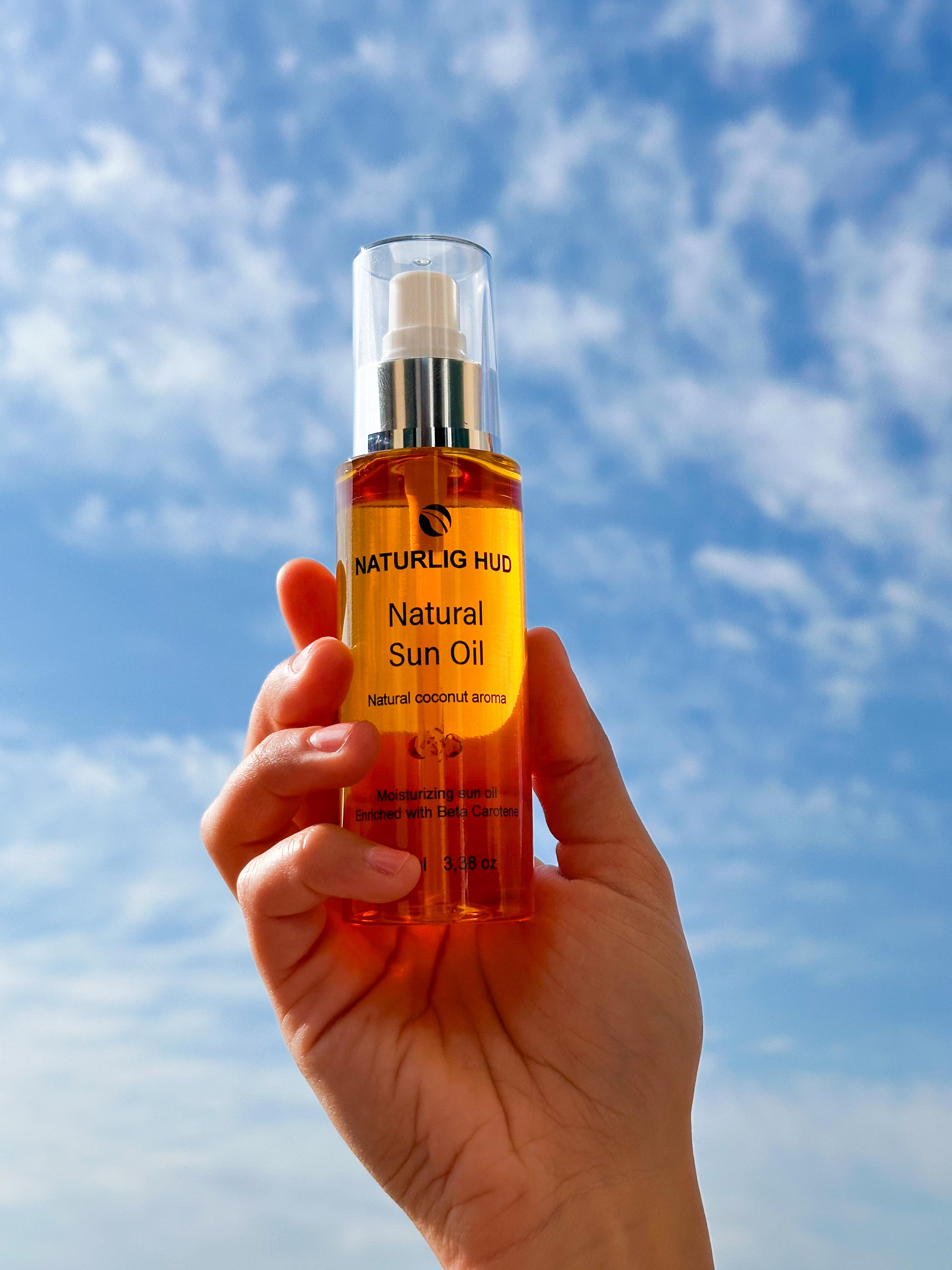 Hand holding a bottle of natural sun oil against a blue sky.