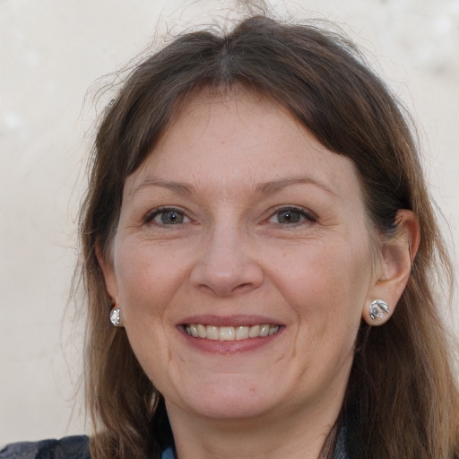 Smiling woman with earrings and long hair, against a neutral background.
