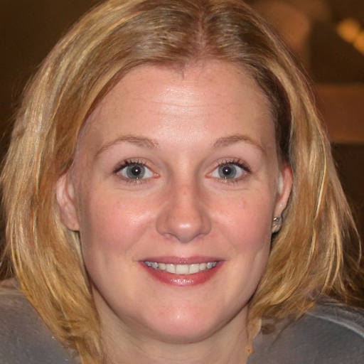 Portrait of a smiling person with short blonde hair and a blurred background.