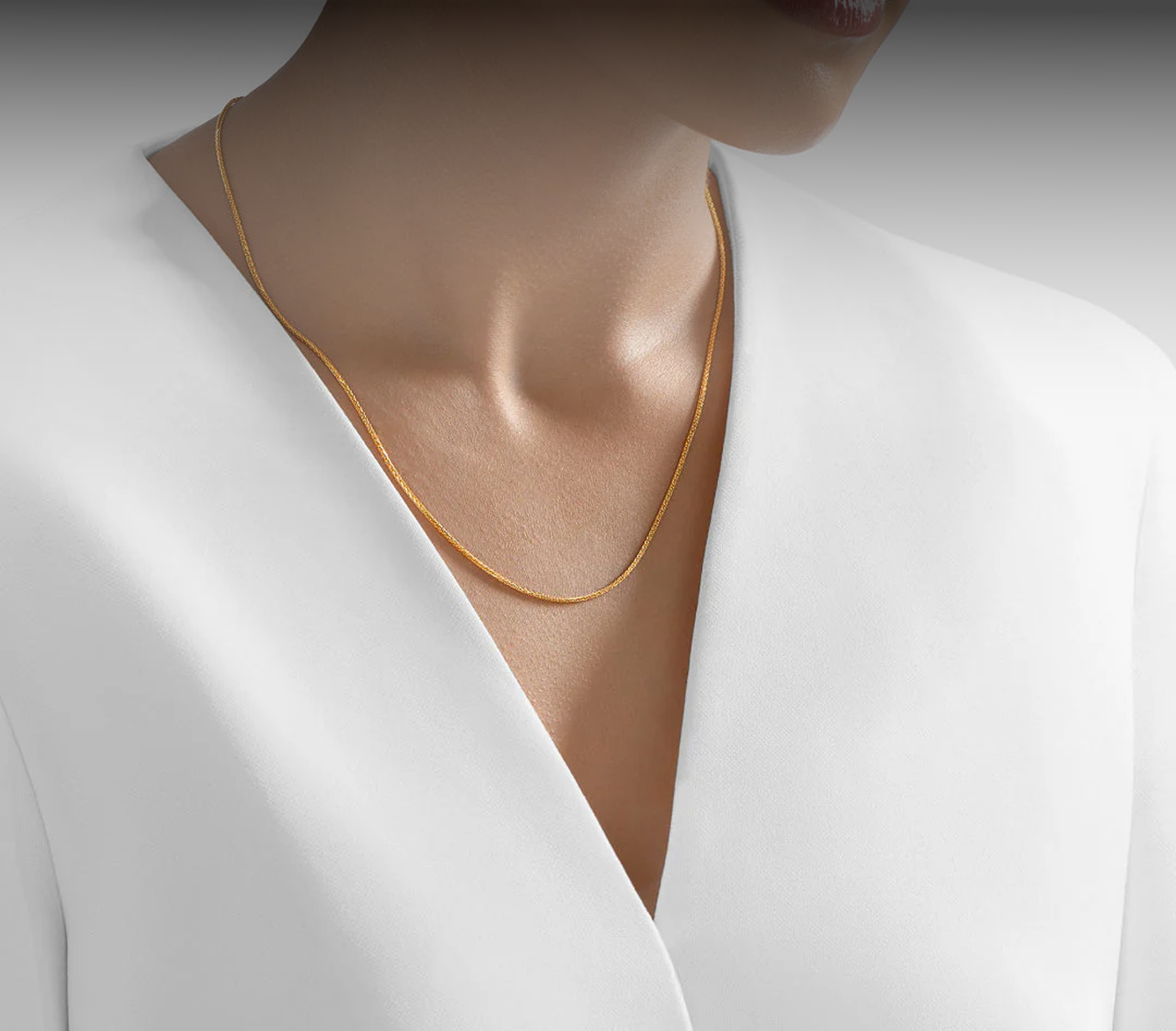 A person in a white jacket wearing a thin gold chain bracelet on their wrist.