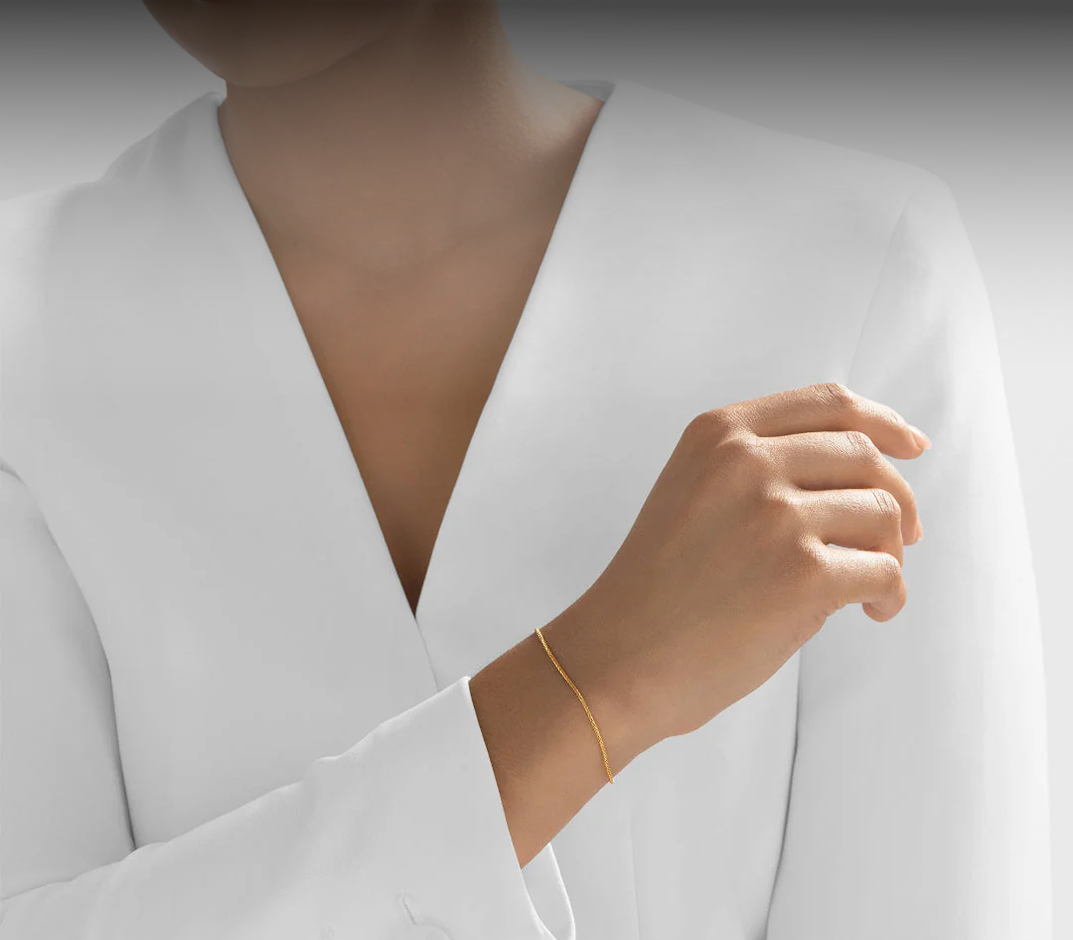 A person in a white jacket wearing a thin gold chain bracelet on their wrist.