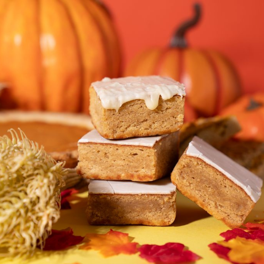 Stack of frosted pumpkin bars with pumpkins and autumn leaves in the background.