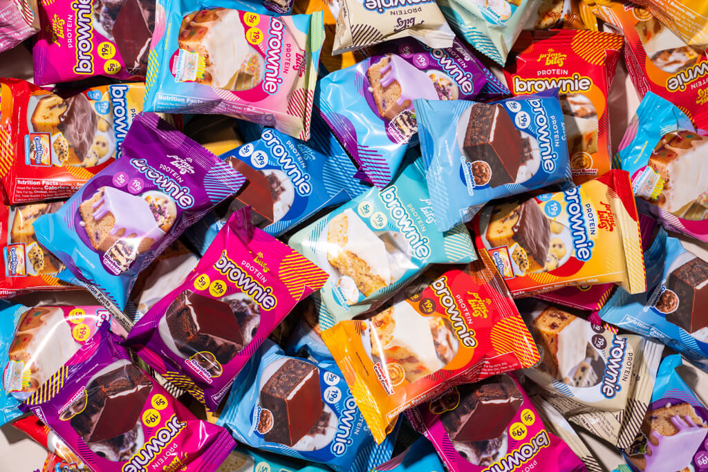 Assorted colorful protein brownie packages scattered randomly.