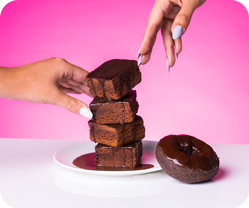Hands stacking chocolate brownies on a plate, with chocolate donut beside.