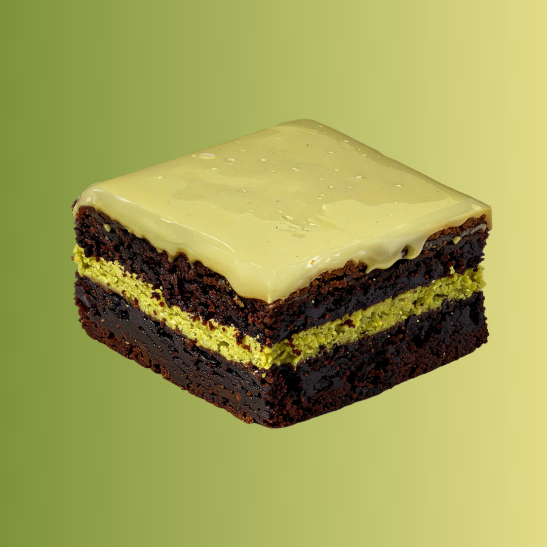 A square, layered brownie with a light green filling and frosting, against a green gradient background.