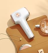 A white and rose gold handheld beauty device rests on a tan purse with cosmetics.