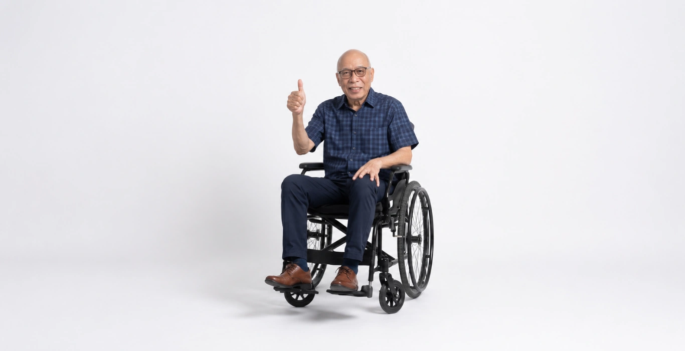An older Asian man in a wheelchair smiles and gives a thumbs up against a white background.