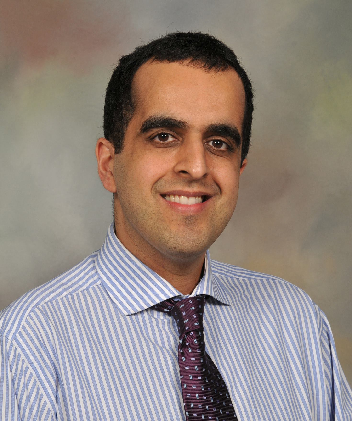 Headshot of a smiling man in a blue and white striped shirt and a purple patterned tie.