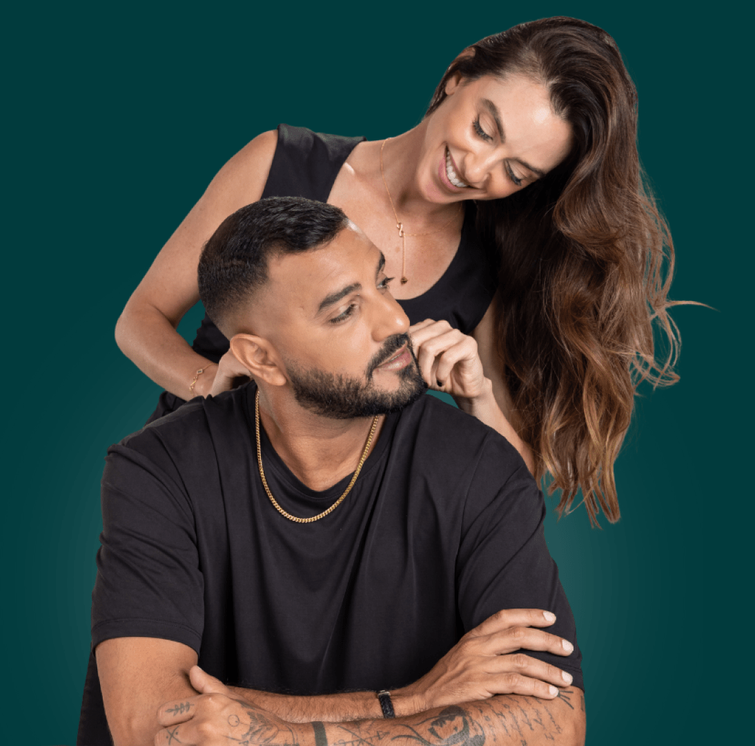 A woman smiling and leaning over a seated man against a teal background.