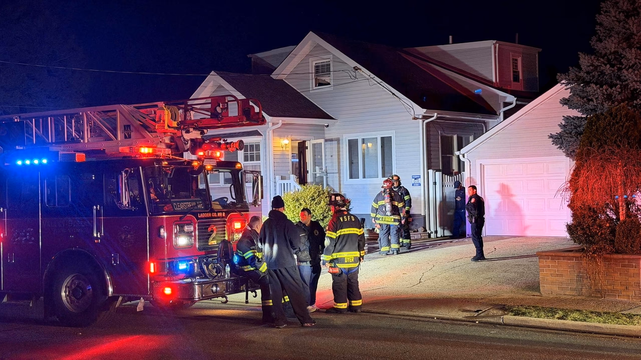 A fire truck and firefighters are gathered outside a house at night with flashing lights.