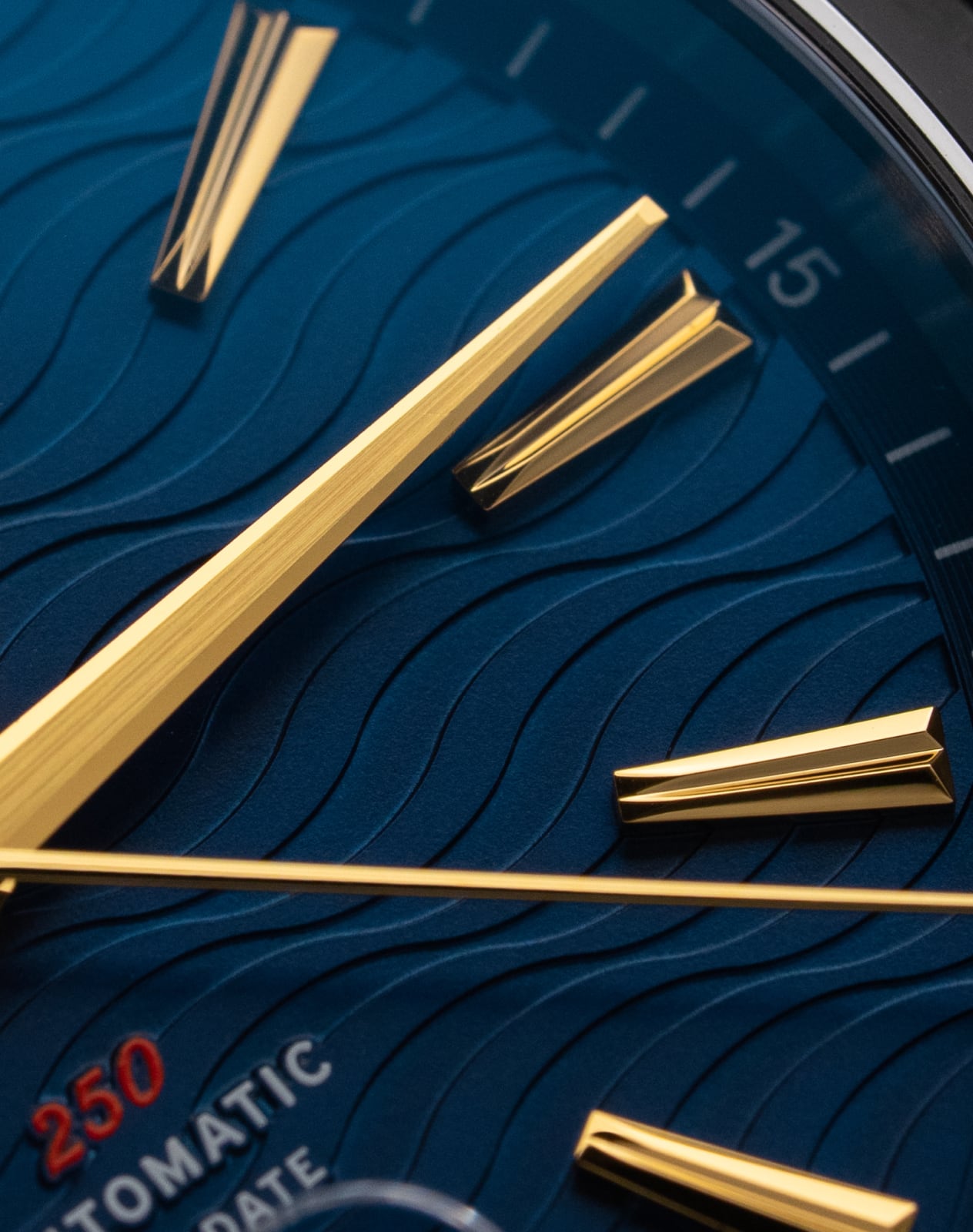 A close-up macro shot of a blue watch face with a wave pattern and gold hands and markers.