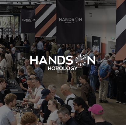 A busy exhibition hall filled with people at the Hands-On Horology event, gathered around display tables.