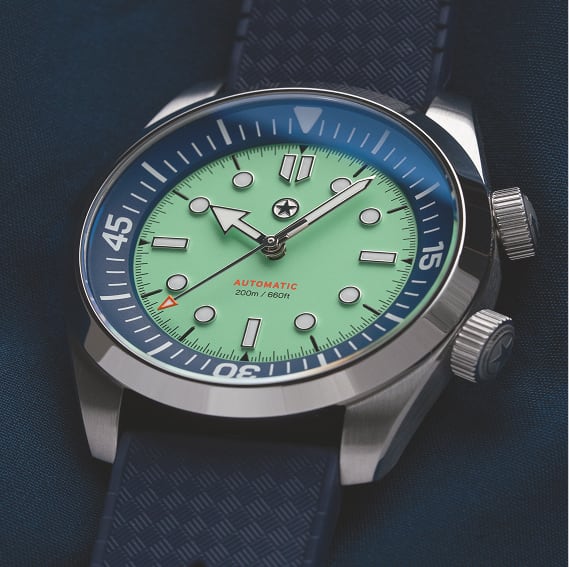 A close-up of a dive watch with a light green face, blue bezel, and a textured blue strap.
