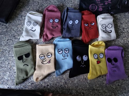 Eleven pairs of colorful socks, each embroidered with a different cartoon face, are laid on a countertop.