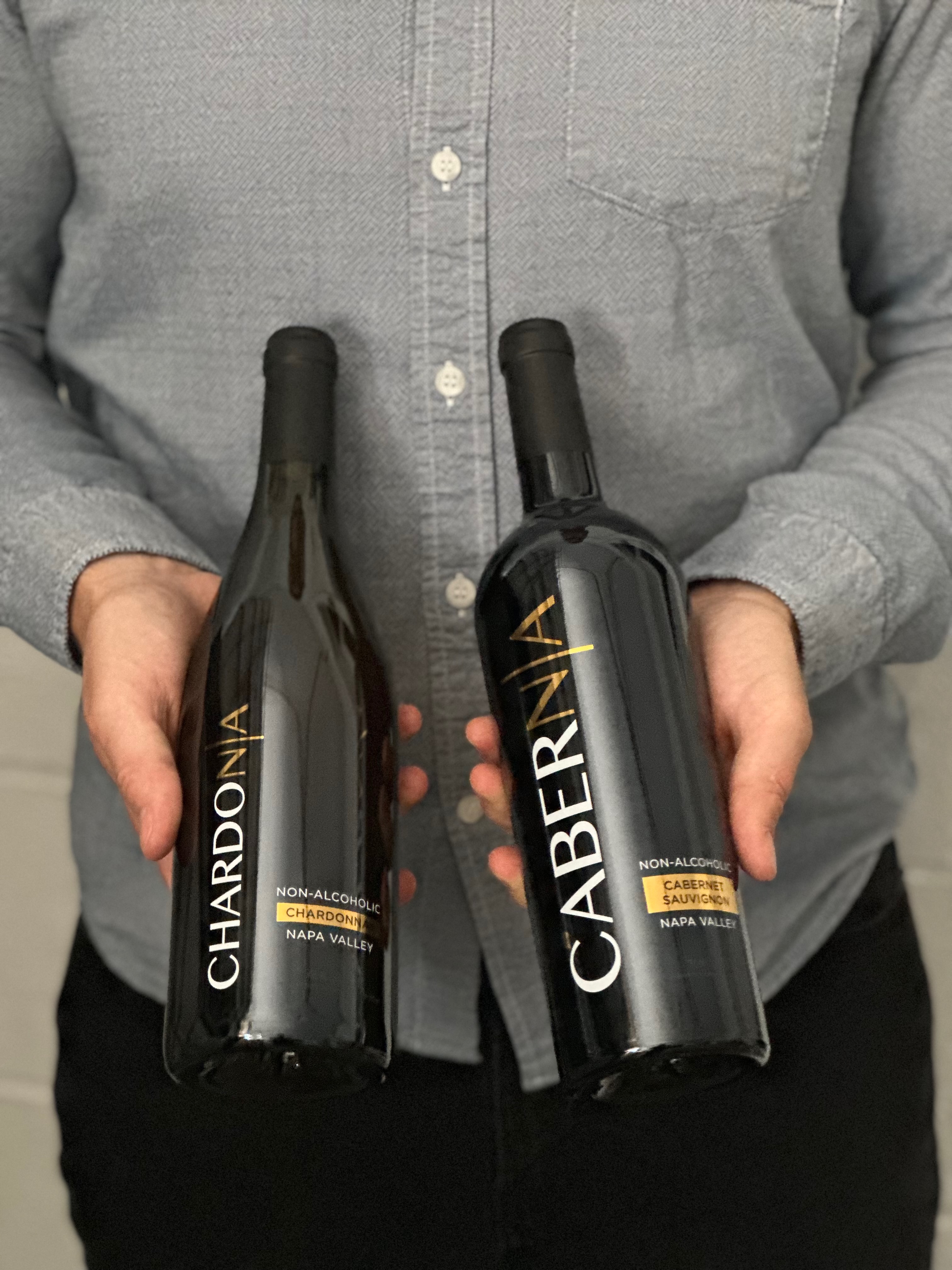 A person holds two bottles of non-alcoholic wine, a Chardonnay and a Cabernet Sauvignon.