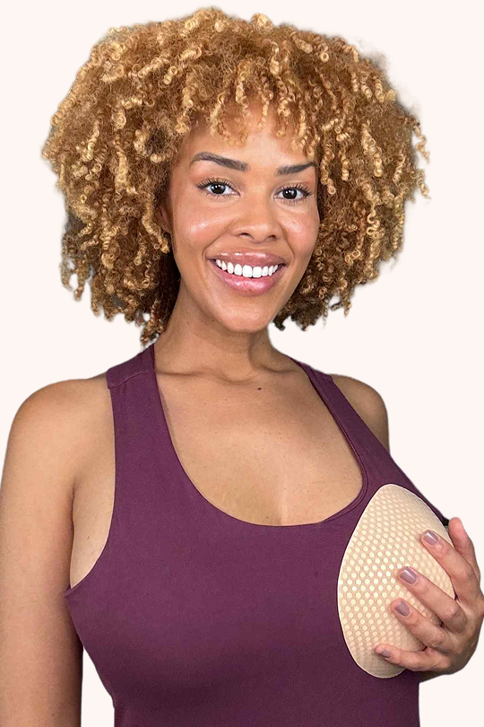 Smiling woman in purple top holding Honey Cloudz water drop bra insert offering smooth full coverage and light shaping, best for tees, everyday bras, and full busts.