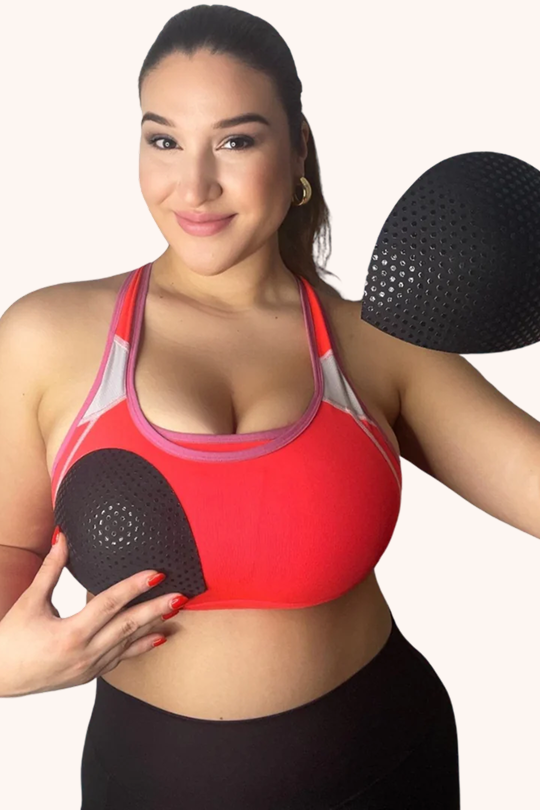 Model in red sports bra holding black Honey Cloudz half moon bra inserts designed for light shaping, nipple coverage, and secure fit for swimsuits and wireless bras
