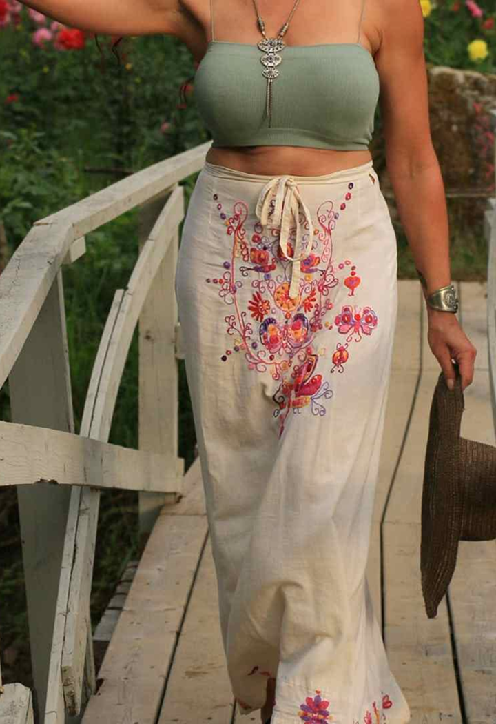 Person in embroidered skirt and green top on a wooden bridge.