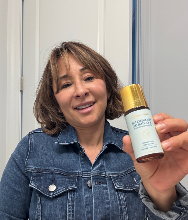 A smiling woman in a denim jacket holds up a small bottle of castor oil.