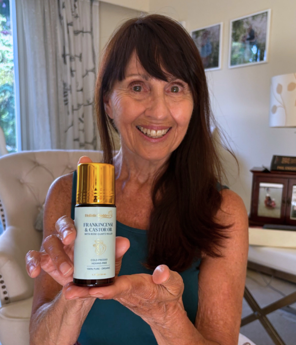 A smiling woman with long brown hair holds up a bottle of Frankincense & Castor Oil.