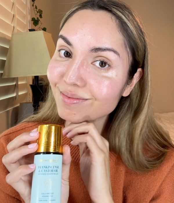 Person holding a bottle of frankincense and castor oil, smiling indoors.