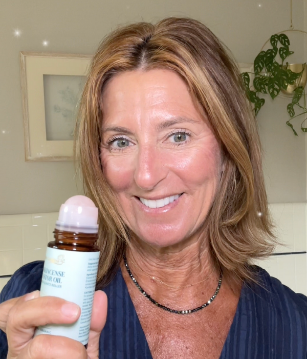 Smiling woman holding a bottle with a roller applicator in a room with plants.