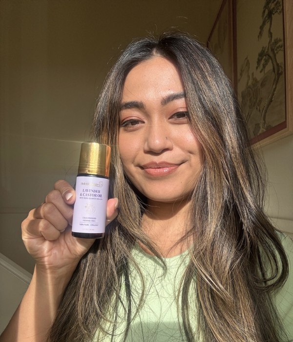 Person holding a bottle of lavender and castor oil, smiling in sunlight.