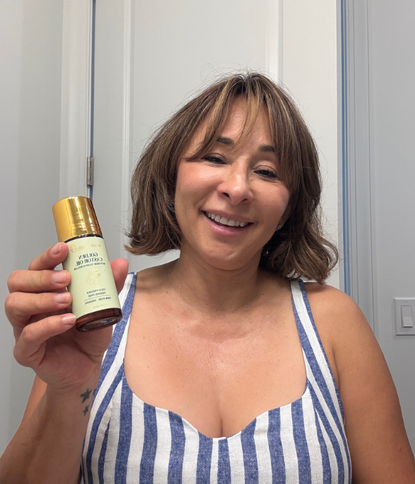 Person smiling, holding a bottle with a gold cap.