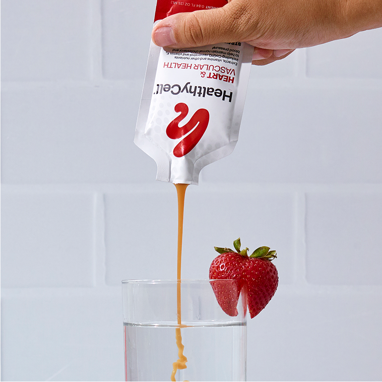 Hand pouring liquid from a pouch into a glass with a strawberry on the rim.
