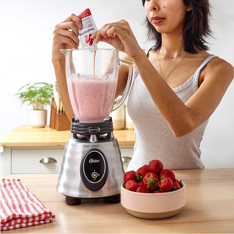 Person adding powder to a blender with pink smoothie, strawberries on the side.