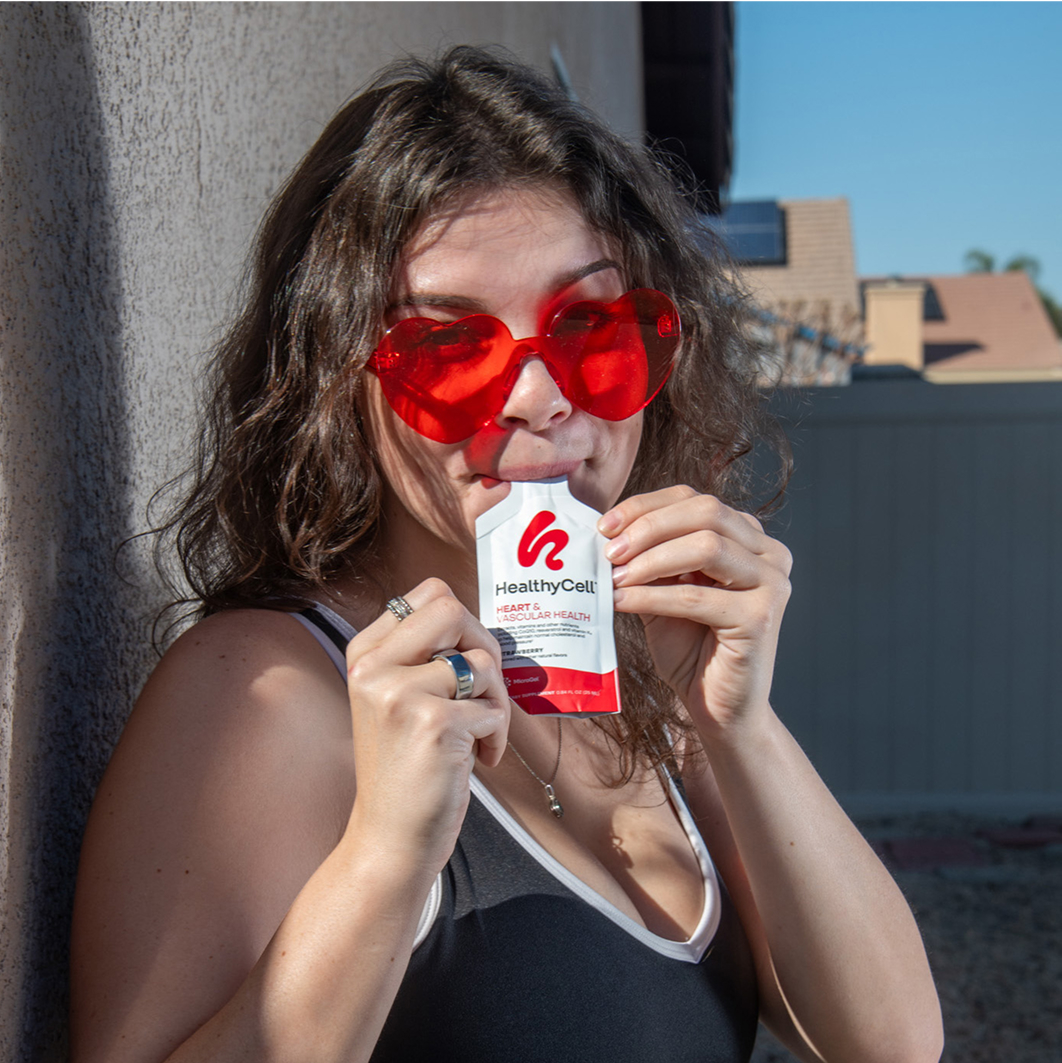 Woman with red heart-shaped sunglasses holding a HealthyCell supplement packet.