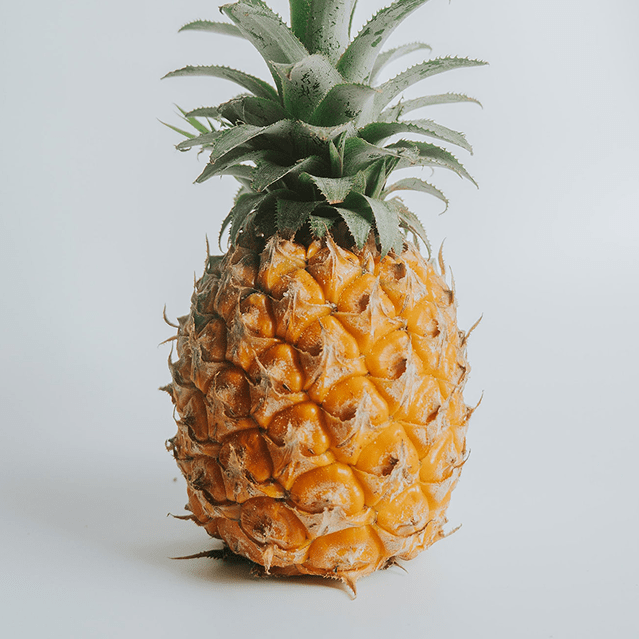 A ripe pineapple with green leaves on a white background.