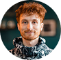 A circular headshot of a young man with curly red hair smiling slightly.