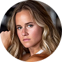 A circular close-up photo of a young woman with blonde hair looking directly at the camera.
