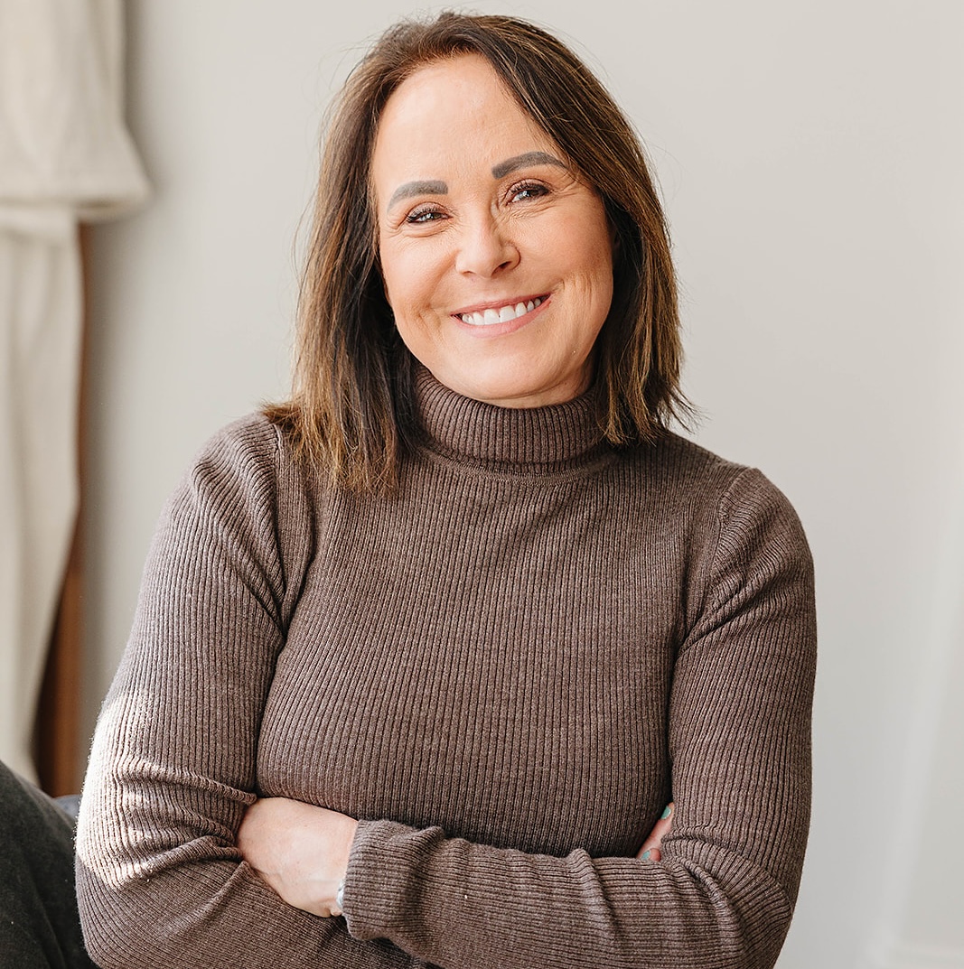 Smiling person in a brown turtleneck sweater with arms crossed.