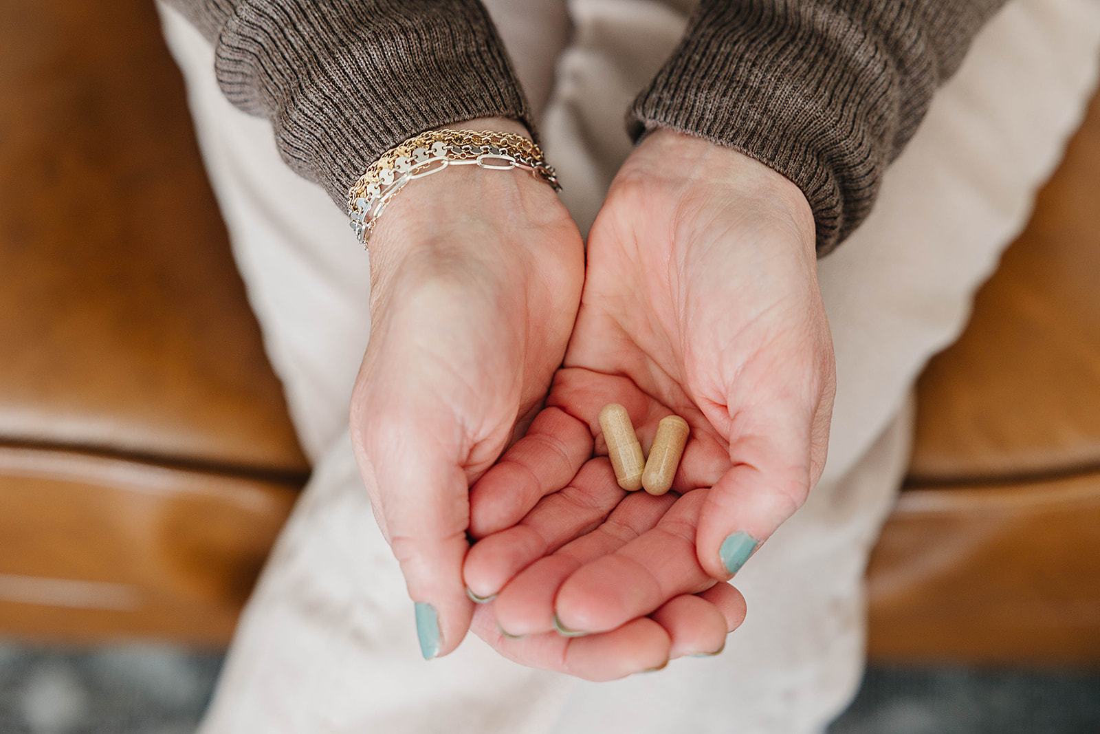 Hands holding two beige capsules.