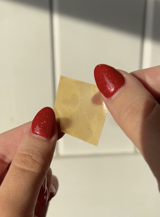 Hands holding a square piece of translucent material with red nail polish.